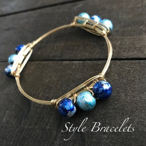 May include: Gold wire bangle bracelet with blue and white agate beads. The bracelet is wrapped with wire and has a simple design.
