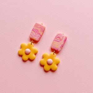 May include: A pair of yellow flower dangle earrings with pink and white marbled rectangle accents.