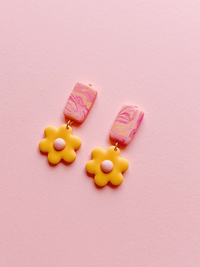 May include: A pair of yellow flower dangle earrings with pink and white marbled rectangle accents.