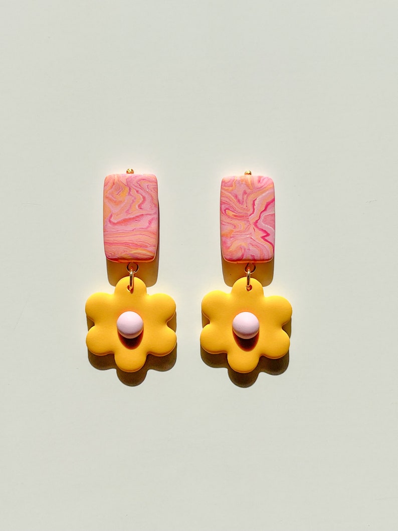 May include: A pair of dangle earrings with a pink and yellow marbled rectangle and a yellow flower with a pink center.