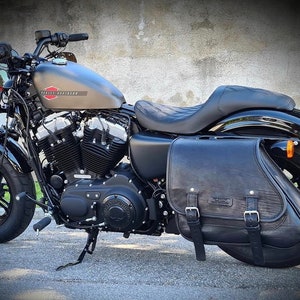 Può includere: Motocicletta Harley Davidson nera con una borsa in pelle nera sul lato destro. La motocicletta ha una sella nera e uno scarico cromato.