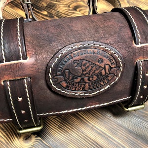 May include: Brown leather motorcycle saddlebag with white stitching and a brass buckle. The bag has a circular logo with the text "Bikers Special Service" and "Paci Quality Leather Motorcycles".