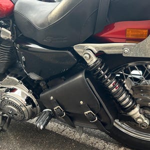 Könnte beinhalten: Ein rotes und schwarzes Motorrad mit Chromakzenten. Das Motorrad hat einen schwarzen Ledersitz, eine schwarze Ledertasche und einen silbernen Motor. Die Räder sind schwarz mit silbernen Speichen.