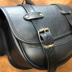 May include: A pair of black leather motorcycle saddlebags with buckles and stitching.
