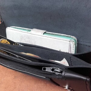 May include: A black leather wallet with a zipper closure and multiple compartments. The wallet is open and shows a white leather phone case inside.