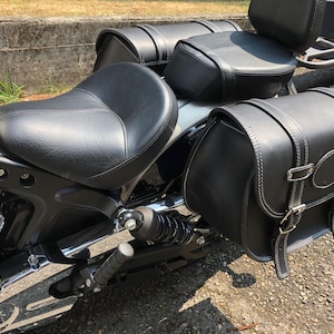 May include: A black leather motorcycle seat with two black leather saddlebags attached to the back of the motorcycle.