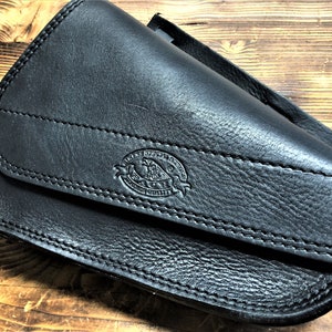May include: Black leather motorcycle saddlebag with a stitched flap and a small embossed logo that reads "Leather Specialists Co. Guaranteed Quality".