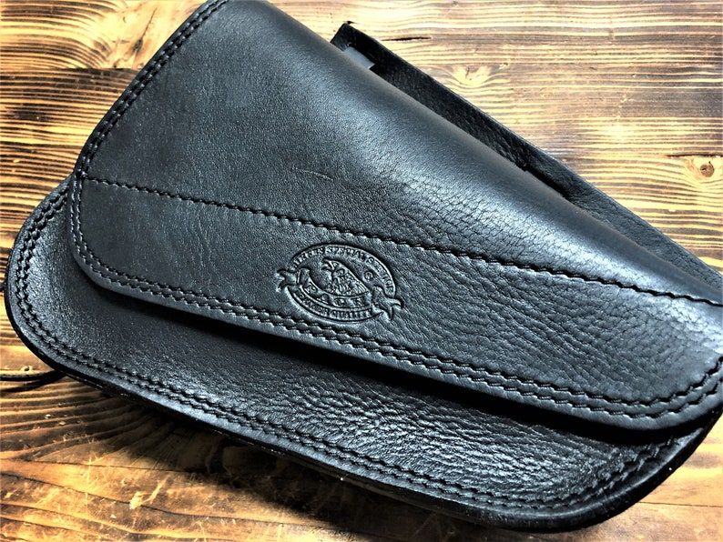 May include: Black leather motorcycle saddlebag with a stitched flap and a small embossed logo that reads "Leather Specialists Co. Guaranteed Quality".