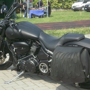 Może przedstawiać: Czarny motocykl z czarnym skórzanym siedzeniem i sakwami. Sakwy mają wzór płomieni.