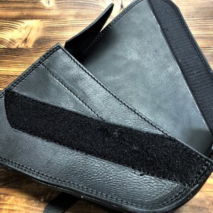 May include: Black leather motorcycle saddlebag with a velcro strap closure. The bag is folded open to show the interior.