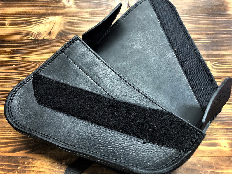 May include: Black leather motorcycle saddlebag with a velcro strap closure. The bag is folded open to show the interior.