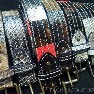 以下が含まれることがあります： 異なるパターンと色の革ベルトが5本。ベルトはヘビ革製で、赤、白、黒の配色。ベルトは白い糸で縫い合わせられ、銀色のバックルが付いている。