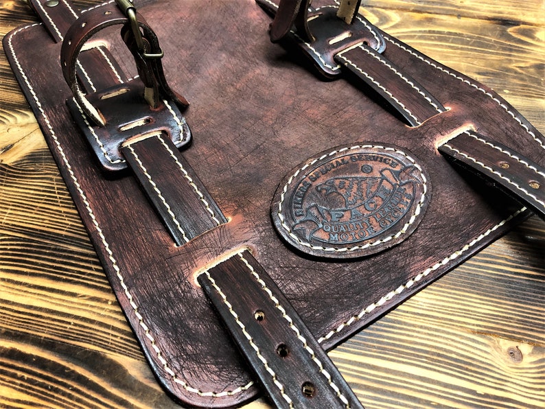 May include: Brown leather motorcycle saddlebags with white stitching and a circular leather patch that reads "HIRES SPECIAL SERVICE QUALITY MOTORCYCLE PARTS".