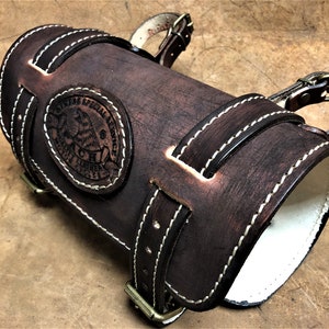 May include: A brown leather arm guard with white stitching and a brass buckle. The arm guard has a circular embossed logo that reads "Owners Special Service" and "Genuine Leather".
