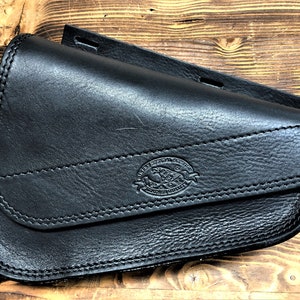 May include: Black leather motorcycle saddlebag with a stitched flap and a logo that reads "Western Saddle Co. Genuine Leather".