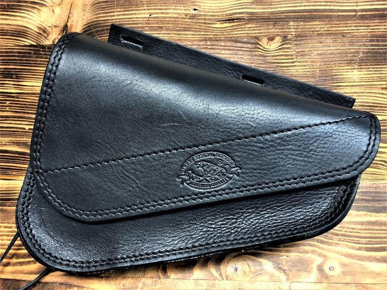 May include: Black leather motorcycle saddlebag with a stitched flap and a logo that reads "Western Saddle Co. Genuine Leather".