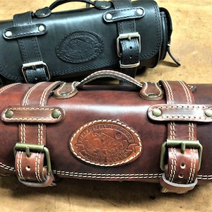 Può includere: Due borse in pelle con fibbie e cinturini. La borsa superiore è nera e la borsa inferiore è marrone. Entrambe le borse hanno un logo che dice "Texas Special Service" con un design di aquila.
