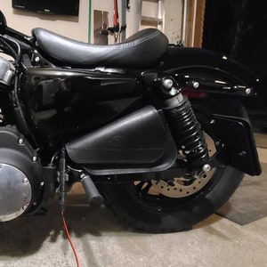 May include: Black motorcycle with a black leather saddlebag attached to the rear fender. The motorcycle has a black seat and a black rear tire.