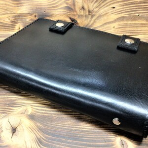 Puede incluir: Un diario encuadernado en cuero negro con detalles metálicos plateados. El diario tiene un acabado liso y pulido y está cerrado.