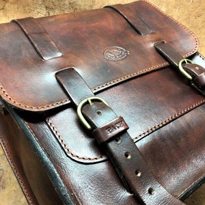 Peut inclure: Un sac de messager en cuir brun avec deux boucles et une boucle en laiton. Le sac a un design cousu et le mot "PATH" est embossé sur la sangle.