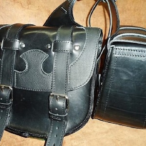 May include: Two black leather motorcycle saddlebags with buckles and straps. The larger bag has a decorative design on the front.