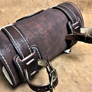 May include: A brown leather arm guard with white stitching and two adjustable straps with buckles.