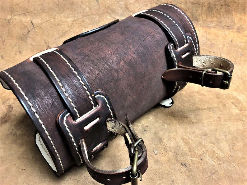 May include: A brown leather arm guard with white stitching and two adjustable straps with buckles.