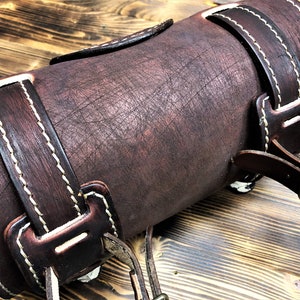 May include: A brown leather motorcycle saddlebag with white stitching and a buckle closure.