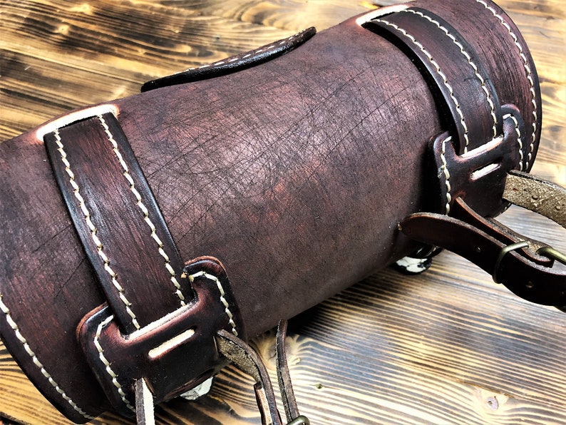 May include: A brown leather motorcycle saddlebag with white stitching and a buckle closure.