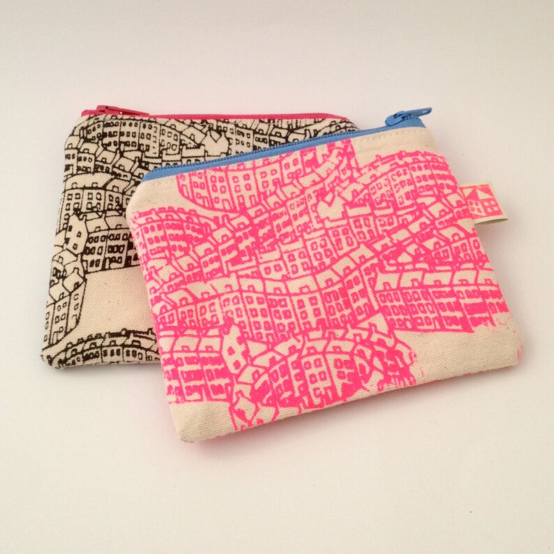 May include: Two small zippered pouches with a city skyline design. One pouch is black and white, the other is white with a pink city skyline.