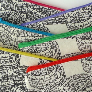 May include: Five zippered pouches with a black and white print of a city skyline. The pouches are lined with different colored zippers: red, purple, blue, green, and yellow.