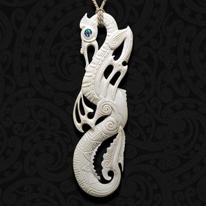 以下が含まれることがあります： クリーム色の骨製ペンダント。複雑な彫刻が施されており、タツノオトシゴのようなデザインです。ペンダントには、小さな虹色の青と緑の象嵌が施されています。自然色のコードで吊り下げられており、暗い背景が特徴です。