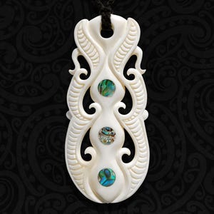 May include: An off-white, elongated pendant featuring intricate, symmetrical carved scrollwork patterns. Three circular, iridescent abalone shell inlays are vertically aligned along the center of the piece. A black cord passes through the top hole.