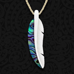 Op de afbeelding: Een ketting met een veervormige hanger. De veer is in tweeën verdeeld, de ene helft wit en de andere met een iriserend abalone schelpenpatroon. De hanger hangt aan een beige koord, tegen een donkere achtergrond.