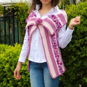 May include: A pink and white striped crochet vest with a flower embellishment. The vest has a loose fit and is made with a textured yarn.