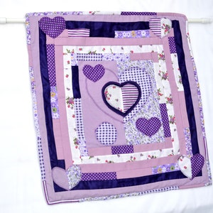 May include: A purple and white patchwork quilt with a heart design. The quilt is made of various fabrics with different patterns, including polka dots, stripes, and floral prints.
