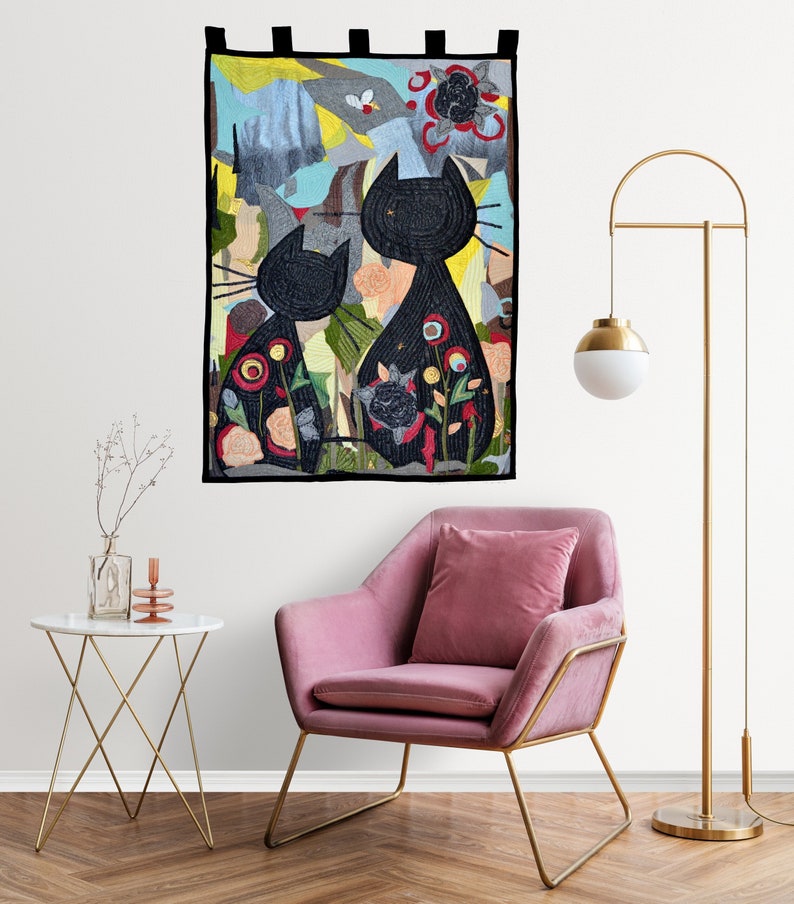 Pode incluir: Uma tape&ccedil;aria de gatos pretos com duas silhuetas de gatos, cada uma adornada com padr&otilde;es florais. O fundo apresenta um design abstrato colorido com tons de azul, amarelo e cinza. A tape&ccedil;aria &eacute; emoldurada com uma borda preta e tem la&ccedil;os pretos para pendurar.