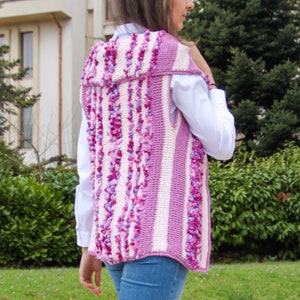 May include: A pink and white striped crocheted vest with a textured, fluffy design. The vest has a hood and is sleeveless.
