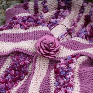 May include: A pink and white striped crocheted blanket with a large pink fabric flower with a pearl in the center.
