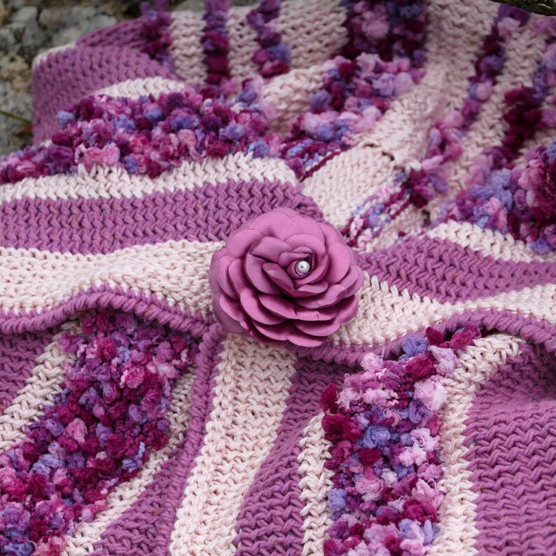 May include: A pink and white striped crocheted blanket with a large pink fabric flower with a pearl in the center.
