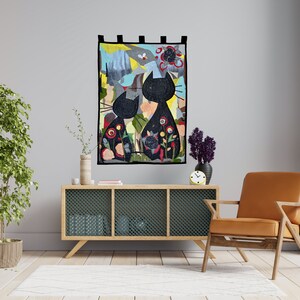 Pode incluir: Uma tape&ccedil;aria decorativa de parede com duas silhuetas de gatos pretos com padr&otilde;es florais e abstratos. A obra de arte est&aacute; sobre um fundo colorido com uma borda preta. &Eacute; exibida acima de um arm&aacute;rio de madeira e uma cadeira de couro.