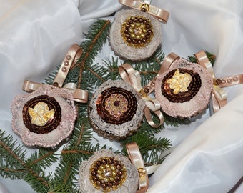 May include: A selection of handmade Christmas baubles. Each bauble is round, with a central design of beads, sequins, or a small angel. They are trimmed with lace, pearls, and ribbons in cream, brown, and gold.