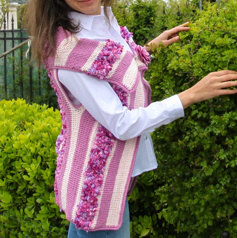 May include: A pink and white striped crocheted vest with a flower embellishment. The vest has a textured, fluffy look.