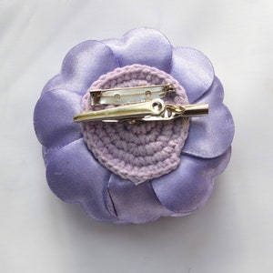 May include: A lavender fabric flower with a crocheted center and a metal pin on the back.
