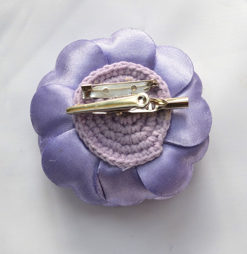 May include: A lavender fabric flower with a crocheted center and a metal pin on the back.