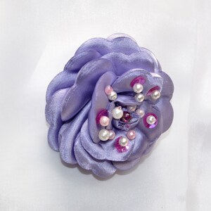 May include: A lavender fabric flower brooch with pink and white pearl accents.