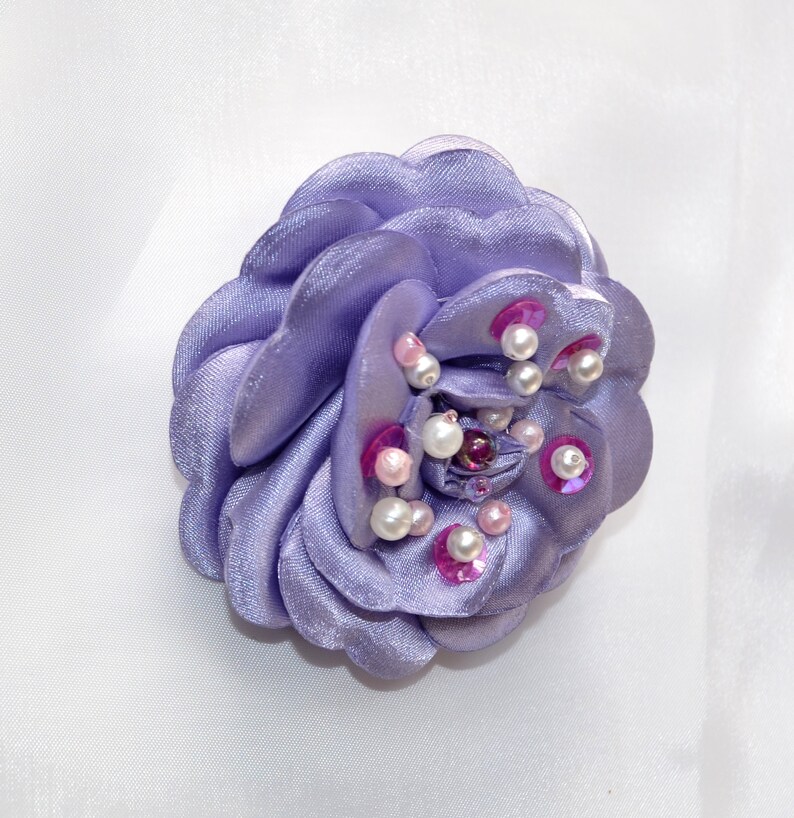 May include: A lavender fabric flower brooch with pink and white pearl accents.