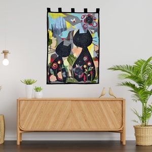 Pode incluir: Uma tape&ccedil;aria decorativa de parede com duas silhuetas de gatos pretos com padr&otilde;es florais. A obra de arte tem um fundo colorido com tons de azul, verde e vermelho. A pe&ccedil;a &eacute; retangular e tem la&ccedil;os de tecido preto na parte superior para pendurar.