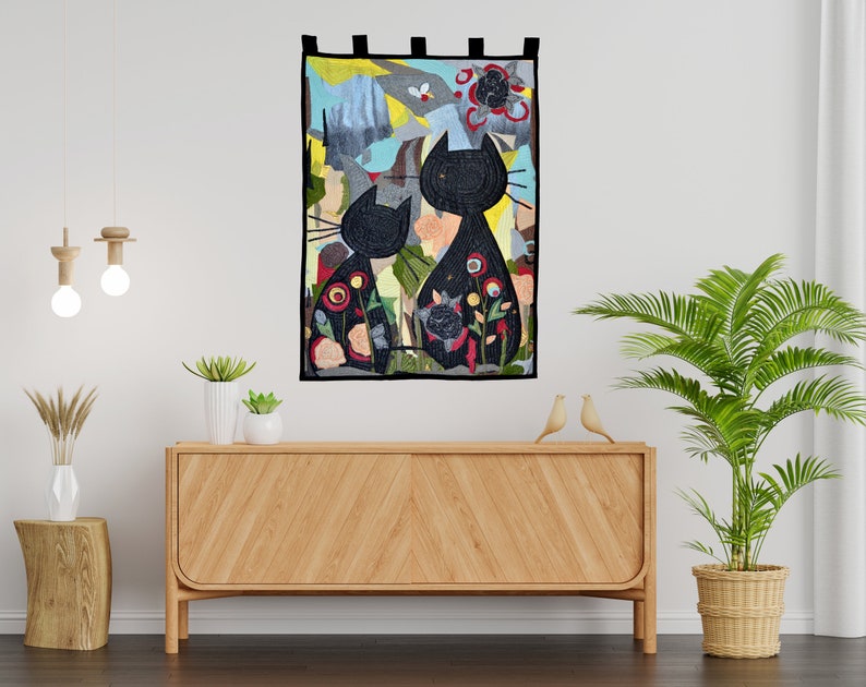 Pode incluir: Uma tape&ccedil;aria decorativa de parede com duas silhuetas de gatos pretos com padr&otilde;es florais. A obra de arte tem um fundo colorido com tons de azul, verde e vermelho. A pe&ccedil;a &eacute; retangular e tem la&ccedil;os de tecido preto na parte superior para pendurar.