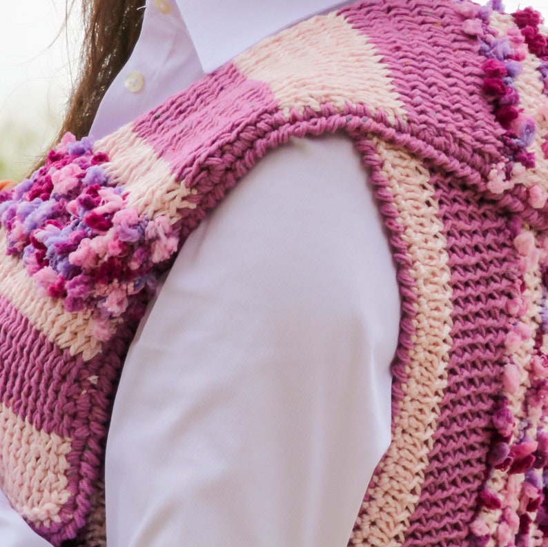 May include: A pink and white striped knitted vest with a textured design and pink pom-poms.
